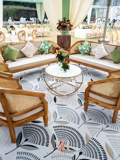 A comfortable and stylish lounge area for a Mehndi. The seating combines natural cane furniture with plush cushions, set on a modern, patterned floor, perfectly capturing the Indo-bohemian vibe.