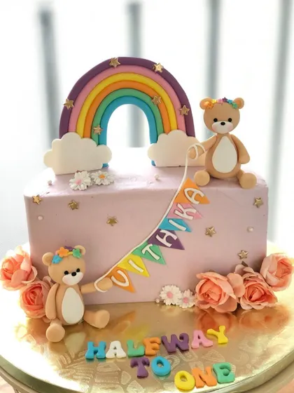 A "Halfway to One" cake with two teddy bears, a rainbow, and fresh flowers.