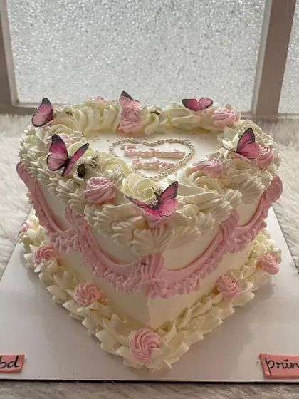 A beautiful heart-shaped vintage cake with pink and white piping and delicate butterflies. It's a design fit for a princess.