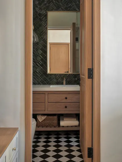 In this master bathroom, we opted for a custom chequerboard floor and arranged jade green tiles in a herringbone pattern for the standout wall. Gold-finish sanitary fittings from Kohler elevate the entire setting.