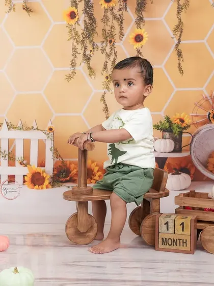 Celebrating 11 months with a sunny sunflower theme. This little one is enjoying his ride on a wooden tricycle in a cheerful, yellow setting.