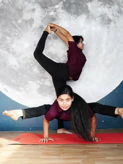 A stunning two-person pose combining an arm balance with a backbend, set against our moon mural. This is where yoga becomes art.