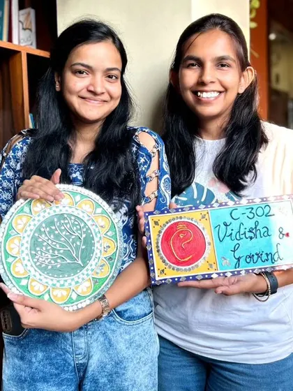 Two participants with their finished Lippan art pieces. One created a nameplate and the other a decorative mirror.