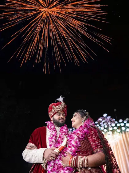 A spectacular shot of the couple with fireworks lighting up the night sky behind them, a perfect end to a grand wedding celebration.