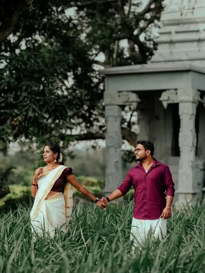 A couple holds hands in a green field, with a historic temple in the background. The composition creates a sense of story and destination.