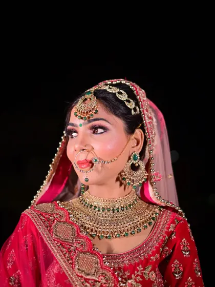 A close-up of the bride looking away with a gentle smile, highlighting her elaborate green and gold bridal jewelry.