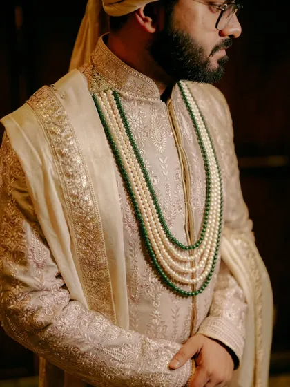 A detailed shot of the groom's attire, focusing on the layered pearl and emerald necklace against his embroidered sherwani.