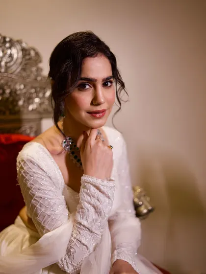 A close-up portrait in the white lehenga, focusing on the soft makeup and the intricate emerald necklace.