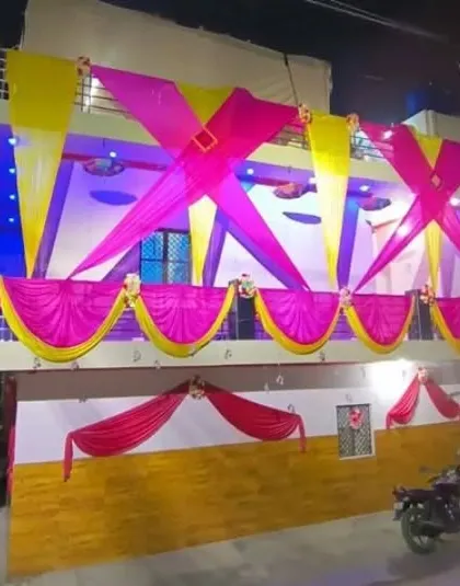 A house facade decorated at night with pink and yellow drapes in a criss-cross pattern, illuminated by blue and purple lights.