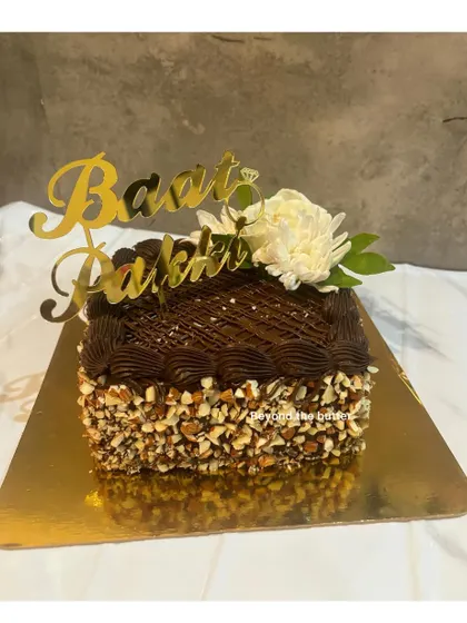 Even a simple chocolate almond cake can be perfect for a "Baat Pakki". This square cake is rich in flavor and elegantly topped with a single white flower and a custom gold topper.