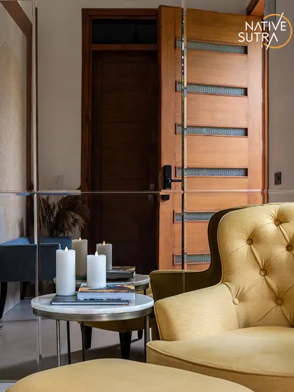 The entrance foyer of Villa Tranquility, where a chic yellow armchair and side table create an inviting experience. The mirrored wall reflects the intricate details of the space, adding depth and warmth.