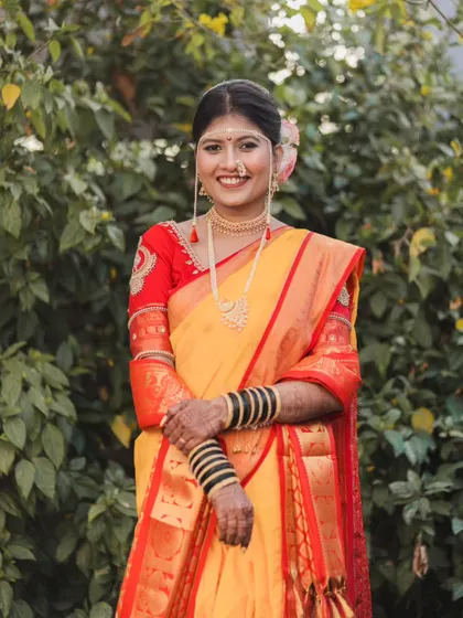A classic portrait of the bride standing amidst lush greenery, her traditional attire looking vibrant and beautiful.