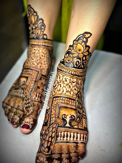 A bride's look is complete only when her feet are adorned with beautiful mehndi. Here is a close up of an intricate bridal foot design, featuring traditional jharokha windows, peacocks, and delicate jaali work, perfectly matching the hand design.