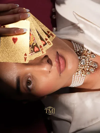 An artistic shot featuring the Polki and pearl choker with a model holding a fan of golden playing cards.