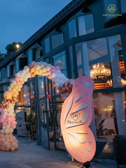 A closer look at the entrance arch, highlighting the large, illuminated butterfly wing prop and the cascading balloon garland.