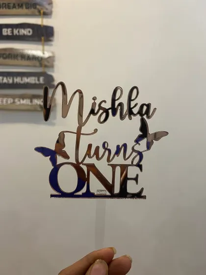 This "Mishka Turns ONE" topper in rose gold features delicate butterfly accents, perfect for a whimsical and gentle first birthday theme.