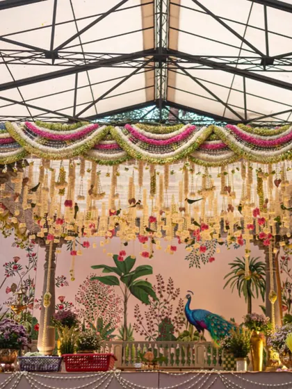 A full view of the traditional South Indian mandap, showcasing the intricate floral torans, classic temple pillars, and the beautiful hand-painted backdrop. We draped the ceiling in soft green fabric to complement the natural surroundings.