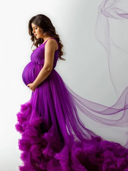 A cascade of royal purple. This gown features a pleated top and a dramatic, heavily ruffled tulle train that creates a stunning ombre effect, perfect for a high-fashion maternity look.