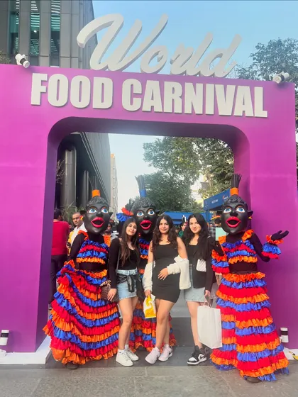 A group of friends poses with performers at the entrance of the World Food Carnival, capturing the excitement and social vibe of the festival.