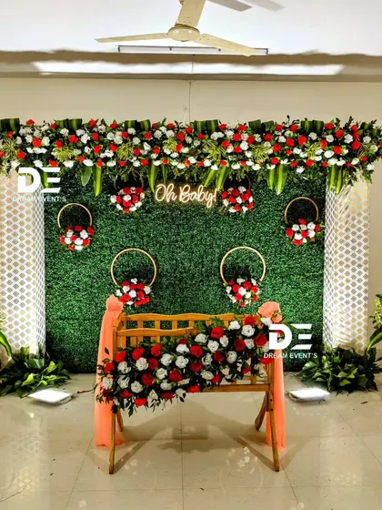A classic and elegant naming ceremony setup for a home. We used a green foliage wall, white lattice panels, and beautiful red and white floral arrangements on the cradle and as accents.