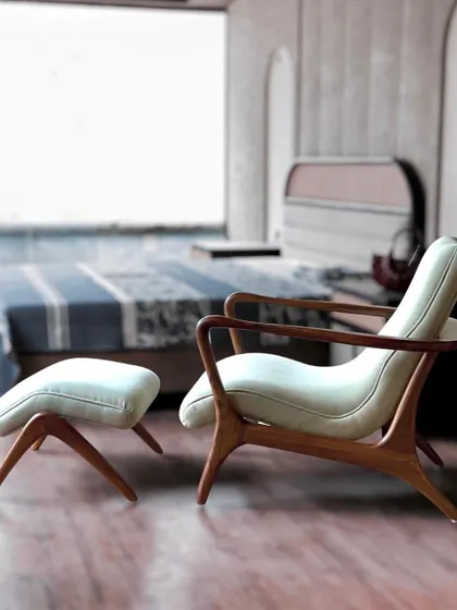 This custom-made lounge chair and ottoman set features a beautifully curved teak wood frame. The smooth, sculptural lines of the wood and the light-colored upholstery make it a perfect addition to a serene bedroom corner.