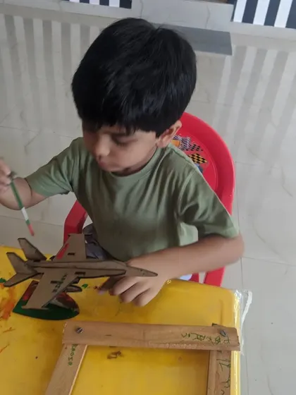 A close-up shot of a child carefully painting his wooden airplane model. This kind of focused activity is great for developing concentration.