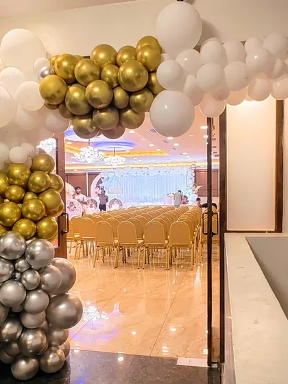 An elegant balloon arch in white, gold, and silver frames the entrance to the main party hall.