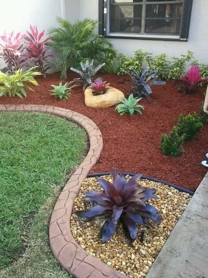 A carefully designed garden bed using red mulch, river pebbles, and a variety of colorful foliage plants like crotons and bromeliads. I use different textures and colors to create visual interest in small spaces.