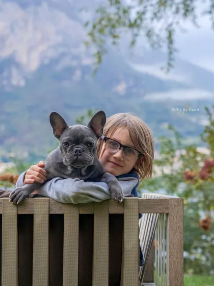 The bond between a boy and his French bulldog puppy is just the sweetest. I love this shot of them peering over the railing, with the gorgeous mountain scenery creating a stunning backdrop.
