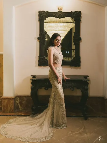 A full-length portrait of Anmol, showcasing the intricate details of her gown against a classic interior. The lighting is focused to create a soft yet striking image.