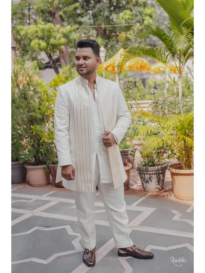 The groom's full look for the pooja. The custom-made white kurta is paired with a matching striped jacket, creating a layered and sophisticated traditional outfit.