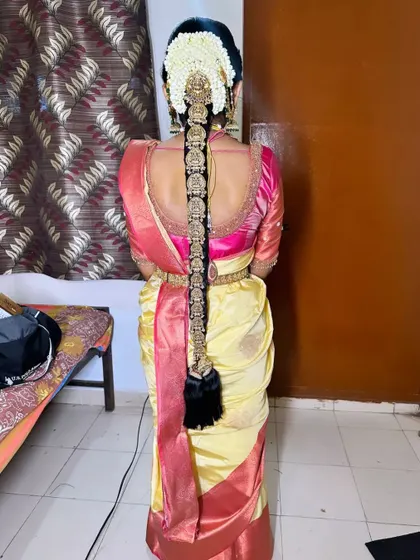 A full length view of a bride's hairstyle, showcasing a traditional gold 'Jadai' that perfectly matches her gold and pink Kanjeevaram saree.