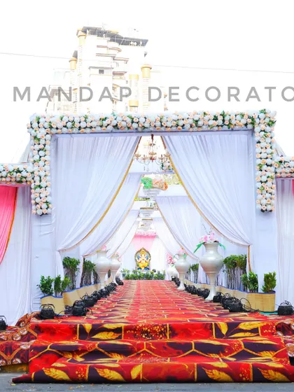 A classic and elegant wedding entrance. The walkway is framed by a beautiful arch of white flowers, with flowing white drapes and chandeliers creating a grand passage for guests.