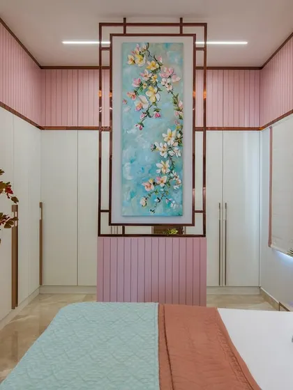 This Indian contemporary bedroom is designed for a daughter, blending playful pastels with sophisticated elements. The room features a pink upholstered bed, floral wallpaper, and a unique partition that doubles as a dressing table, creating a space that is both beautiful and functional.