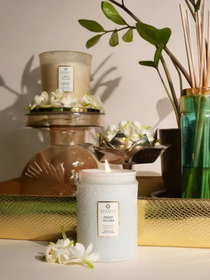 The pure, clean scent of Fresh Mogra, captured in our hand-poured candles. The elegant white engraved jar and the lit candle on a golden tray create a scene of pure tranquility and luxury.