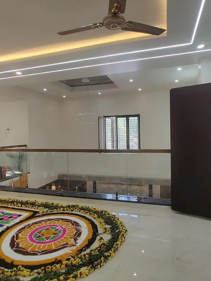The upper living space decorated for a housewarming ceremony with a traditional rangoli. The large sliding doors open to a spacious terrace, blending indoor and outdoor spaces.