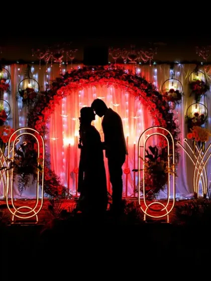 A dramatic silhouette of the couple against their stunning, red-themed reception stage decor.