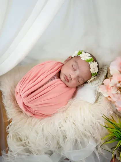 Wrapped in a soft pink swaddle, this baby sleeps under a delicate white canopy. The pink blossoms in the foreground add a lovely, soft touch to the composition.