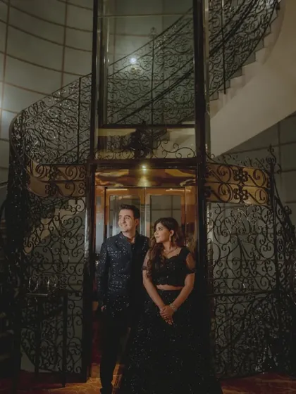A grand, stylish portrait of the couple in front of an ornate elevator and spiral staircase.