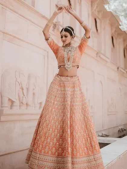 A full-length shot of the peach lehenga, capturing its elegant movement and the beautiful architectural backdrop.