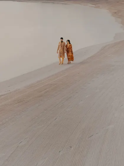 A minimalist and artistic shot of the couple walking across vast sand dunes. This pre-wedding portrait uses the expansive landscape to create a sense of romance and adventure.