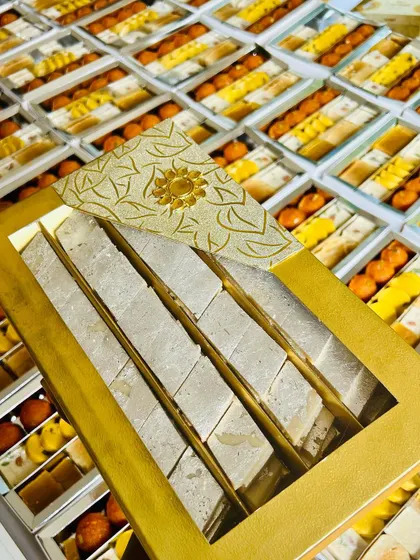 Our premium Kaju Katli, packed in a beautiful gold box, is a top choice for high-end corporate and wedding gifts. The background shows our capacity to handle large volumes for any festive season.