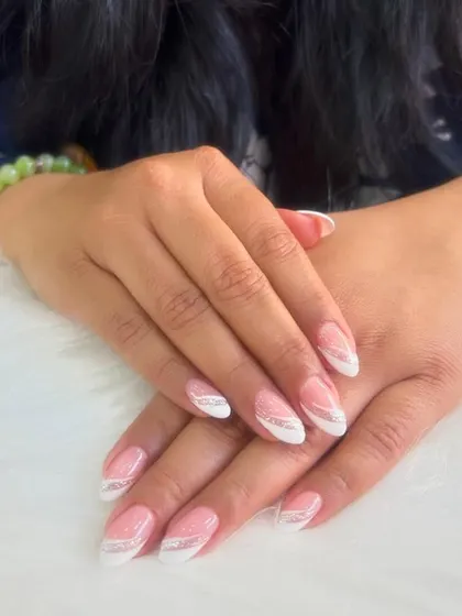 A perfect example of timeless elegance. This design features a classic French manicure with a subtle twist, adding a delicate silver glitter line to accentuate the clean white tips on almond-shaped nails.