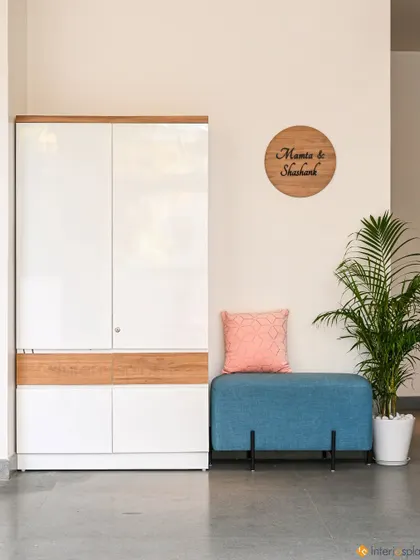 This foyer area features a sleek white and wood shoe cabinet, a comfortable blue bench for seating, and a personalized wooden nameplate on the wall.