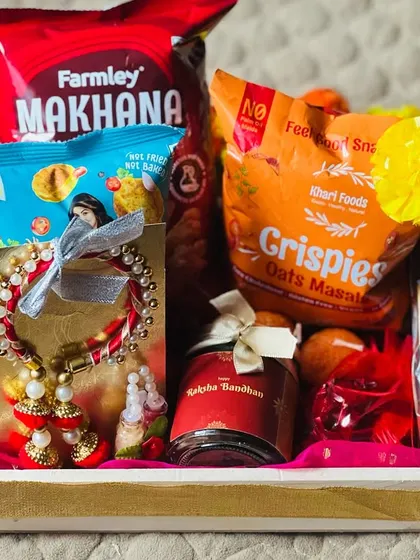 A Rakhi hamper in a wooden tray, featuring a beautiful bhaiya-bhabhi lumba rakhi set along with snacks.