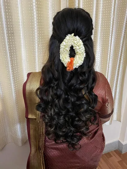 A half-up hairstyle with beautiful, bouncy curls, adorned with a fresh jasmine gajra for a touch of tradition.