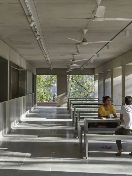 The interior of the CEPT University Canteen features long communal tables and benches made of simple, durable materials. The design creates a functional and robust space for dining and socializing, with natural light filtering in from the open sides.