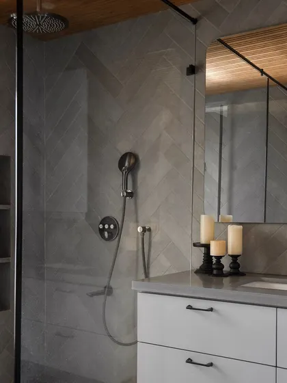 In this modern bathroom, herringbone-patterned grey tiles create a dynamic yet calming shower enclosure. Matte black fixtures add a contemporary edge, while the built-in niche provides elegant, functional storage for daily essentials.