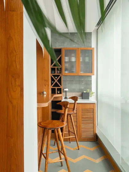 We converted a balcony into this cozy bar nook. The space is fully clad in teak wood, with a built-in wine rack and louvered cabinet doors. The chevron-patterned flooring continues from the main living area, creating a seamless transition.