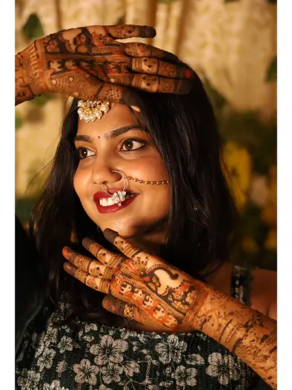 A happy bride framing her face with her beautifully adorned hands. The rich color of the mehendi stain signifies the love and joy of the occasion.